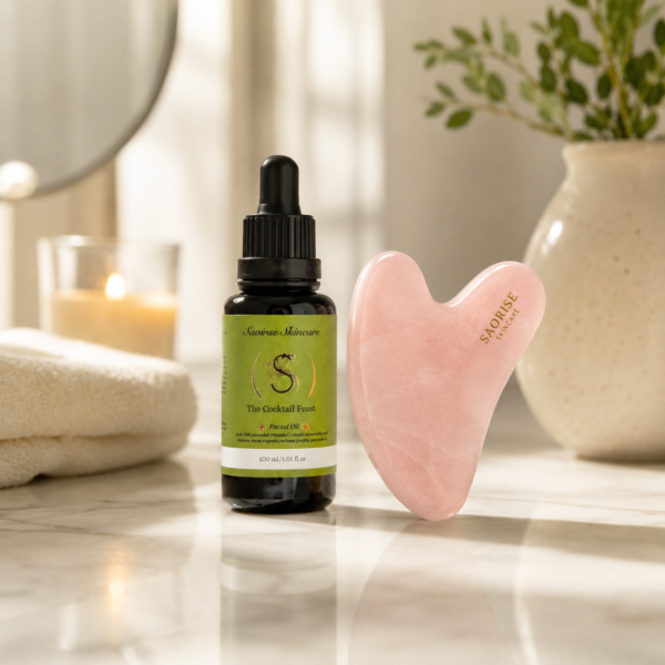 Dark glass dropper bottle with a green label reading 'The Cocktail Feast' beside a pink heart-shaped facial gua sha tool on a marble surface in a spa-like setting
