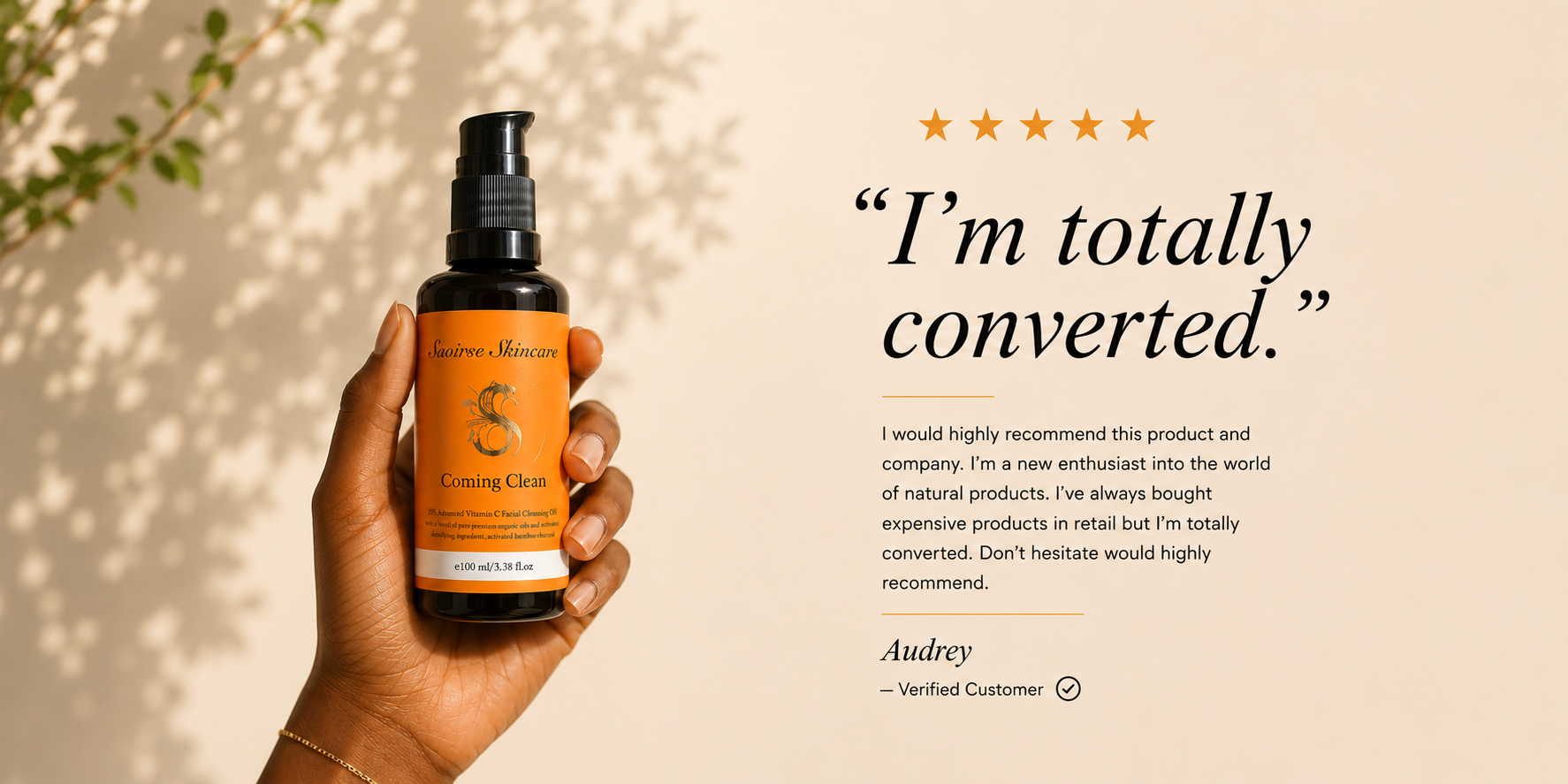 Hand holding an orange spray bottle labeled 'Coming Clean' from Saoirse Skincare, with a beige backdrop and a testimonial on the right.