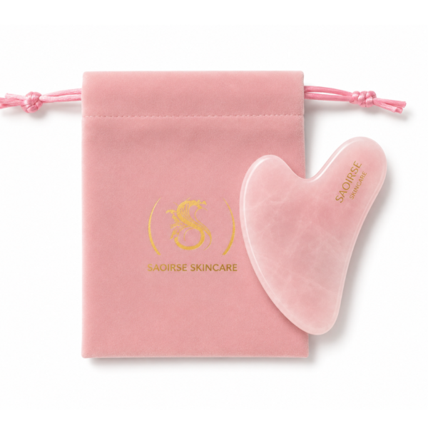 Pink velvet drawstring pouch with gold logo next to a pink heart-shaped gua sha tool from Saoirse Skincare.